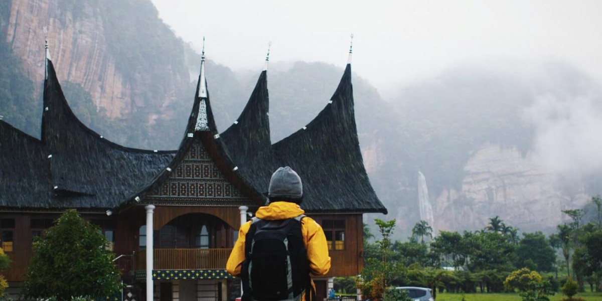 A hiker stands in front of an old asian building. Misty mountains in the background.